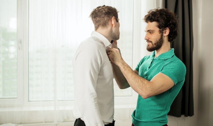 young man helping another young man to button his shirt