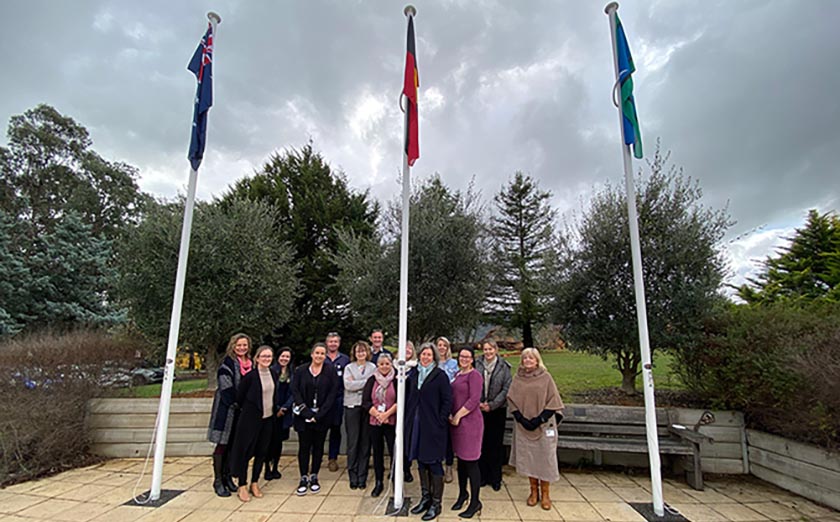 A group of alpine health staff and CHAG standing around three flag poles with the Australian National flag, Aboriginal Flag and the Torres Strait Islander Flag.